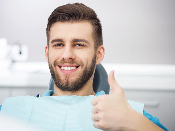 Smiling man in dentist’s chair giving thumbs up