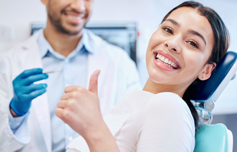 Patient smiling while giving thumbs up in treatment chair